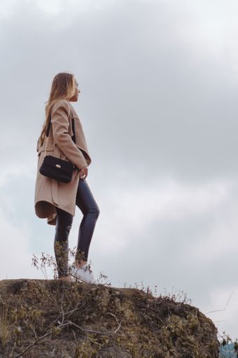 A vertical shot of a young blonde Caucasian woman standing on the top of the hill during a cloudy day