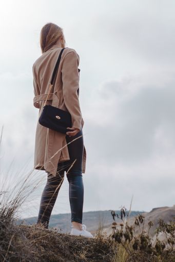 A vertical shot of a young blonde Caucasian woman standing on the top of the hill during a cloudy day