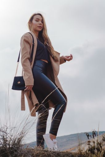 A vertical shot of a young blonde Caucasian woman standing on the top of the hill during a cloudy day