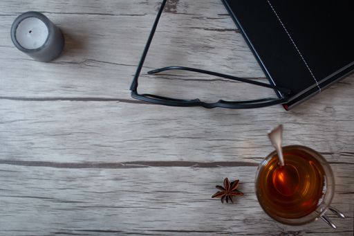 A top view of star anise tee with a black notebook, eyeglasses, and candle on a wooden table