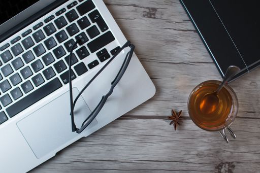 A top view of star anise tee with a black notebook, eyeglasses, and laptop on a wooden table