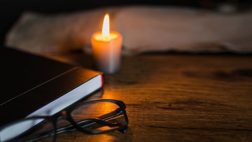 A high angle shot of a black notebook and eyeglasses with a candle on a wooden table
