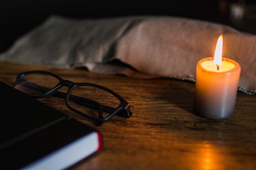 A high angle shot of a black notebook and eyeglasses with a candle on a wooden table