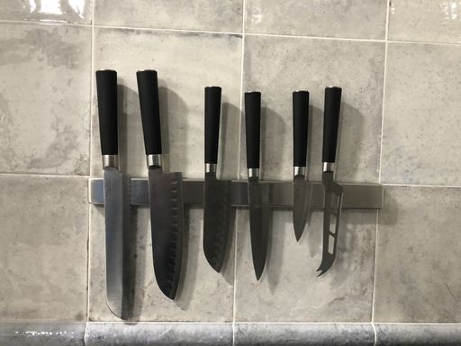 A closeup shot of a magnetic holder with sharp knives on a kitchen til