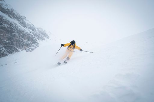 A scenic view of a skier with a yellow ski suit, skiing down a snowy slope