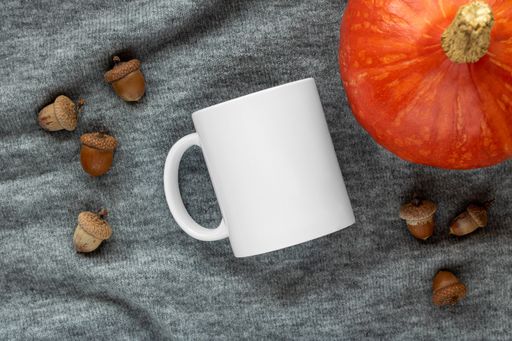 A closeup of a white mug and pumpkin on a gray cloth background