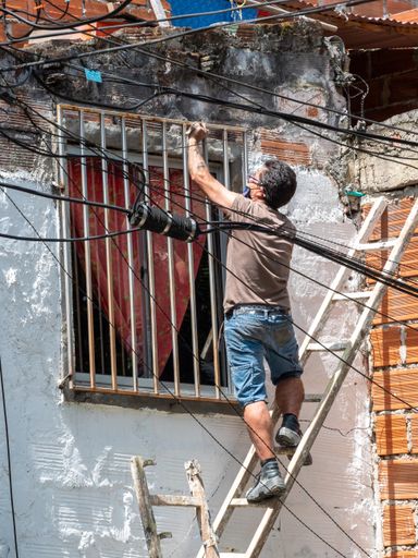 Medellin, Antioquia / Colombia - November 15 2020: Latin Man Climbing a Ladder Puts a Grill on the Window