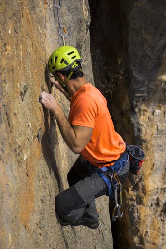 A vertical shot of a person wearing an online t-shirt climbing a rock