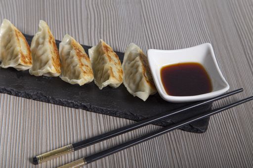 A closeup shot of chicken gyozas served on slate dinnerware with chopsticks and soy sauce