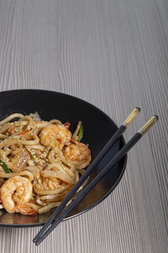 A vertical shot of udon noodles with prawns and vegetables