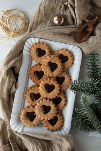 A platter of freshly baked heart-shaped linzer cookies on a rustic kitchen table