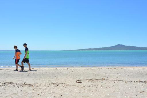 View of two young men walking at St Heliers beach with Rangitoto Island in background
