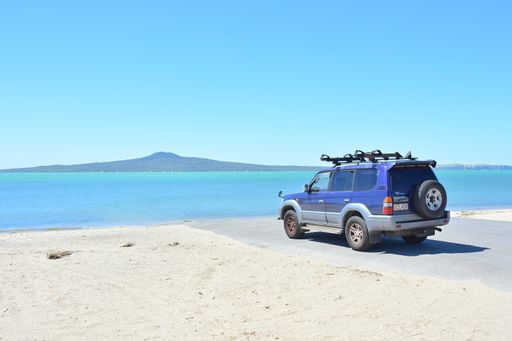 View of blue Toyota Landcruiser Prado parked at St Heliers beach with Rangitoto Island in background