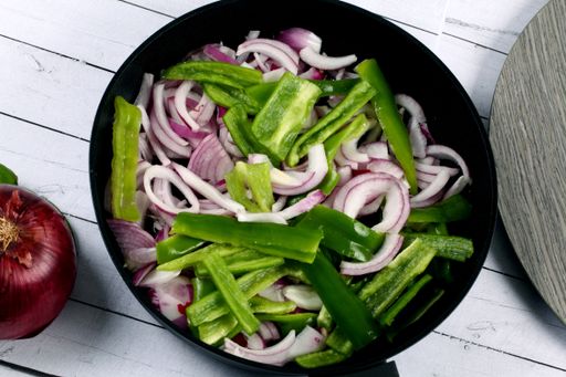 A top view of onions and chili peppers in a frying pan ready to be fried
