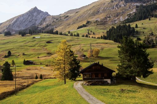 A single-story rural house situated on a lush green hill overlooking a majestic mountain range on a sunny day