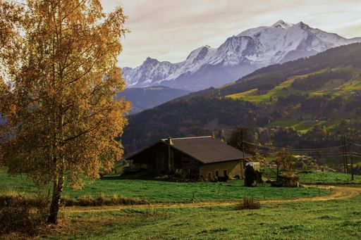 A single-story rural house situated on a lush green hill overlooking a majestic mountain range on a sunny day