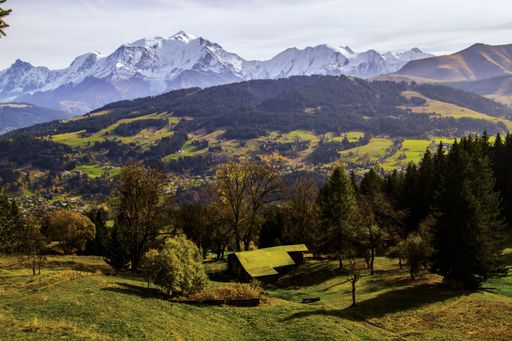 A single-story rural house situated on a lush green hill overlooking a majestic mountain range on a sunny day