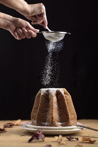 A delicious Pandoro with chocolate filling, a traditional Italian sweet bread, female hands sprinkling the dessert with powder