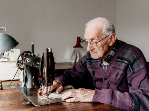 An old man working on a vintage sewing machine on a wooden table
