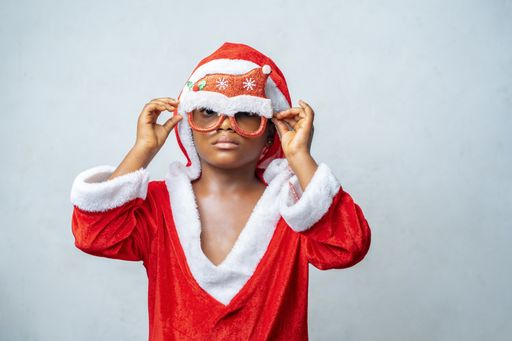 A closeup shot of a black child wearing Christmas themed clothes on a gray background