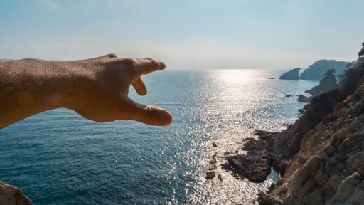 A shallow focus shot of a person's hand pointing to the sea on a sunny day