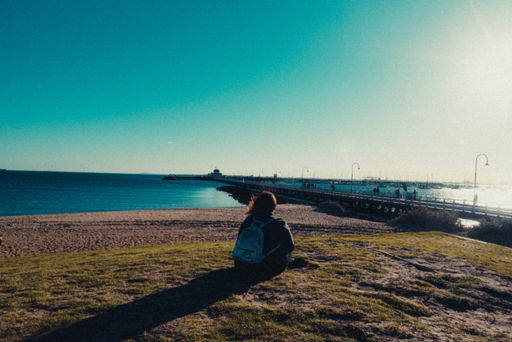A female in a backpack sitting at the coast of the sea near a pier