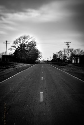 A vertical greyscale shot of a road under the cloudy sky on the countryside