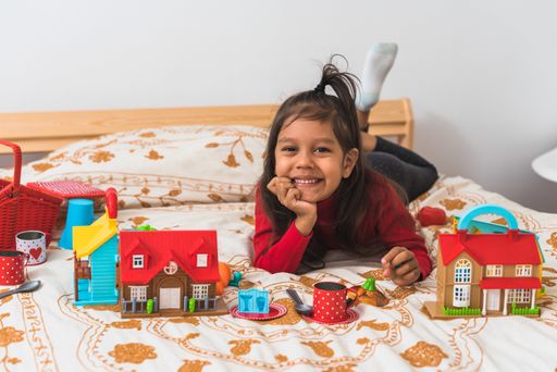 A cute little girl in a red sweater playing with her toys in the bedroom