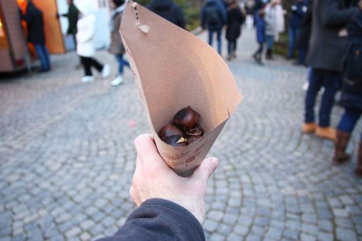A pov shot of a person holding a brown paper bag filled with chestnuts outdoors