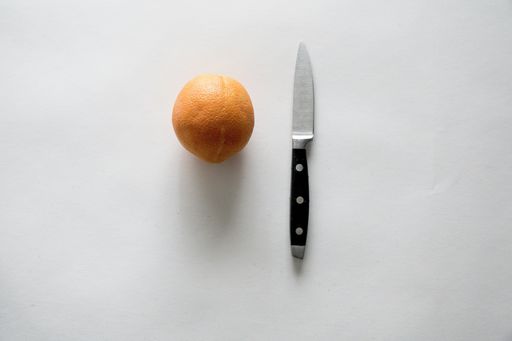A high angle shot of an orange and knife on a white surface