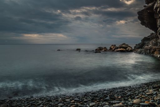 A beautiful view of the wavy sea hitting the rocky beach gleaming under the stormy cloudy sky