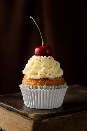 A vertical shot of a delicious cupcake with cream and cherry on top on a book