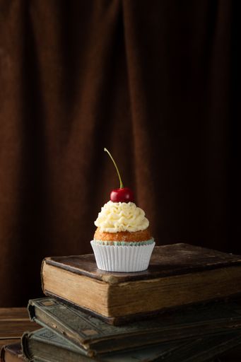 A vertical shot of a delicious cupcake with cream and cherry on top on books