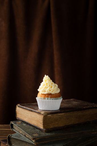 A vertical shot of a delicious cupcake with cream on books
