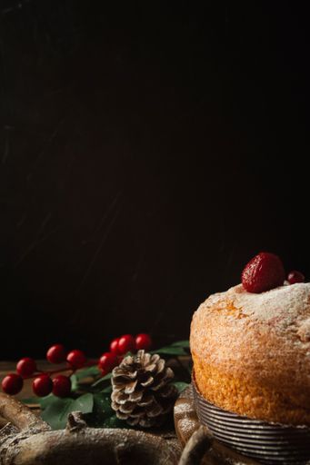 A vertical shot of a delicious sponge cake with strawberries, a pine cone, and redberries on table