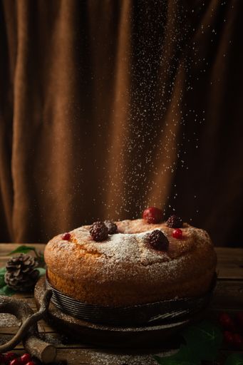 A vertical shot of a delicious cake with powdered sugar, red berries, strawberries, and blackberries