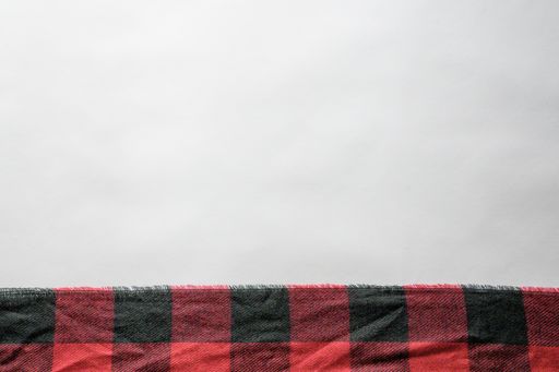 A red and black flannel texture on a white surface with empty space for text