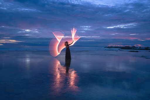 A female light painting model on sandy Tanjung Layar Beach during beautiful dark blue sunrise