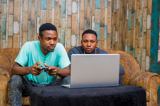 Two young African men playing a video game on a laptop at home