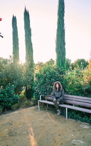 A young caucasian female sitting on a wooden bench in a park at sunset