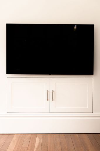 The vertical shot of a modern TV screen over a white cabinet doors on the wall