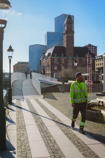 A vertical shot of a man walking on a paved street in Malmo with classic buildings on his background