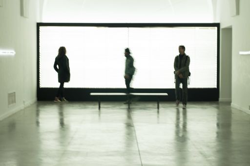A view of three people standing far apart from each other inside of a building