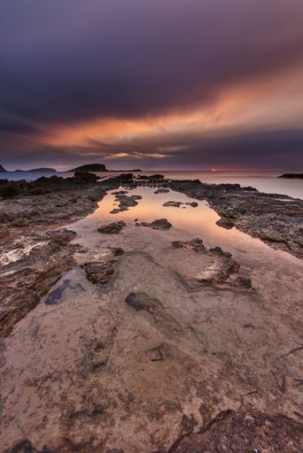 A vertical shot of a beautiful sunset over a rocky lake