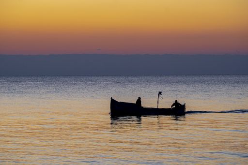 A silhouette of two fishers on a boat fishing at sunset