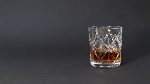 A glass of whiskey on a grey table against a blurry background