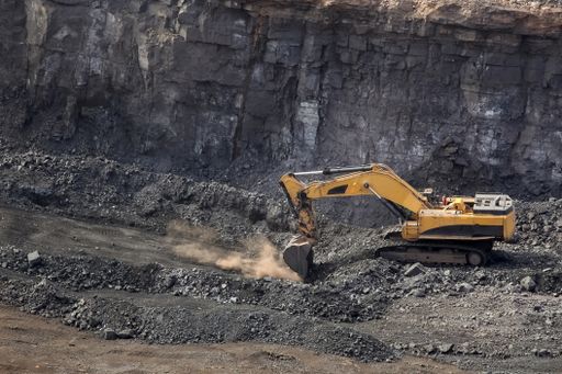 A yellow excavator digging for ore rich rock in an open pit mine