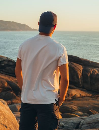 The picture shows a back view of an unrecognizable teenager with your hands in your pockets watching the sea on a sunny afternoon