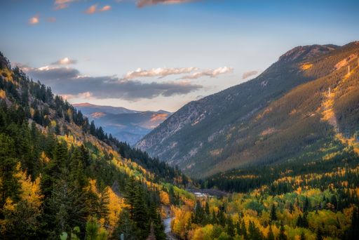 A beautiful scenery of a green landscape with colorful trees surrounded by rocky mountains