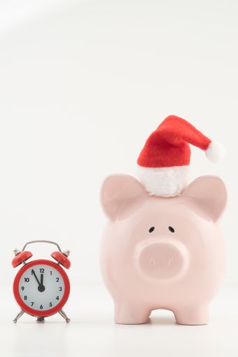 A piggy bank in a Santa Claus hat and an alarm clock isolated on the white background, the "Time is Money" concept, advice for the upcoming year